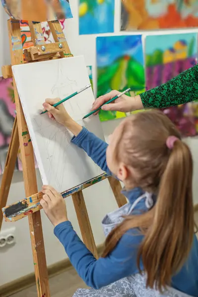 Çeşitli resimlerle dolu canlı sanat sınıfı ortamında tuvale odaklanmış at kuyruğu çizimleri olan bir çocuk..