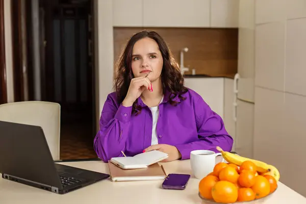 思慮深い学生は ノートパソコン ノートパソコン スマートフォンで彼女のキッチンテーブルに座って 新鮮なフルーツのコーヒーとボウルに彼女の日を計画 — ストック写真