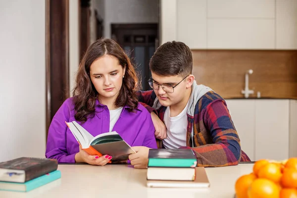 2人の10代の学生が一緒に教科書を綿密に調べ テーブルの上の本の積み重ねで家庭環境での共同研究に従事しています — ストック写真
