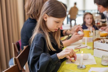 Konsantre genç kız aile atölyesinde geleneksel paskalya yumurtası yapma zanaatı uyguluyor..