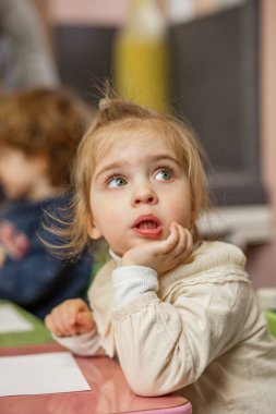 Büyük mavi gözlü küçük kız anaokulundaki bir etkinliğe katılırken düşünceli görünüyor..