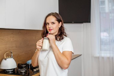 Beyaz tişörtlü kız modern mutfağında ev yapımı muzlu mascarpone smoothie yudumlamayı seviyor..