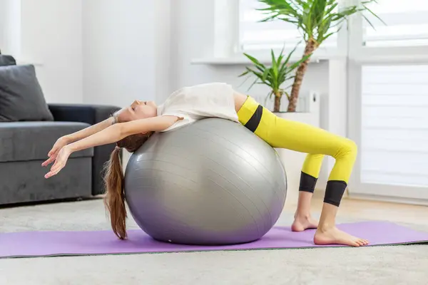 女孩用一个健身球进行仰卧起坐锻炼 在家里的瑜伽垫上伸展胳膊 — 图库照片