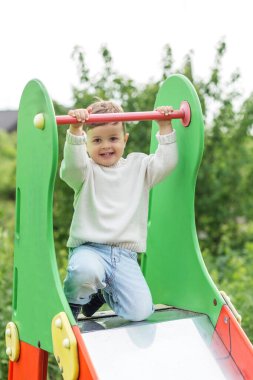Mutlu çocuk renkli bir oyun parkında kayıyor, bara tutunuyor ve dışarıda eğleniyor..