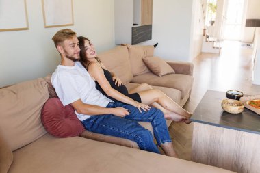 Mutlu hamile kadın ve partneri rahat bölmeli koltukta kahve masasında atıştırıyor, birlikte huzurlu bir anın tadını çıkarıyorlar..