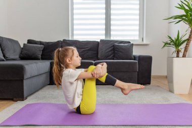 Oturma odasındaki yoga minderine poz veren çocuk, yoga seansı sırasında çekirdek kuvvete, dengeye ve istikrara odaklanıyor..