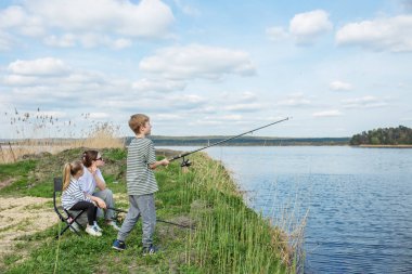 Anne ve iki çocuk, doğa ve açık gökyüzüyle çevrili nehir kıyısında rahatça balık avlamayı severler..