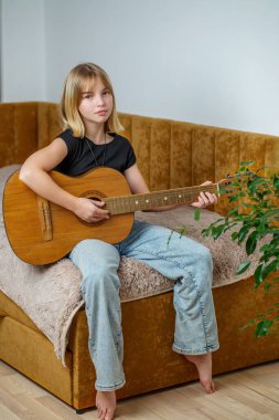 Kısa saçlı genç bir kız sıcak ve davetkar bir oturma odasında bir kanepede otururken akustik gitar çalar ve müzik eşliğinde eğlenir..