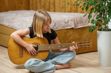 Genç bir kız, öğleden sonra rahat bir yaşam alanında akustik gitar tıngırdatmaktan hoşlanır..