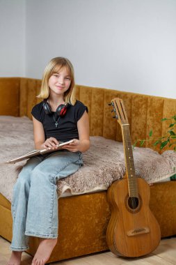Genç bir kız, elinde flüt tutarken müzik defterine odaklanmış bir şekilde bir yatakta rahatça oturur. Yanında bir gitar duruyor, müziğe olan tutkusunu şık, havadar bir odada gösteriyor..