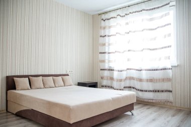 Dekoratif yastıklı, açık renkli duvarlı ve doğal ışığın odayı aydınlatmasına olanak sağlayan perdeli sade bir yatak odası. Mekan modern minimalizmi yansıtıyor..