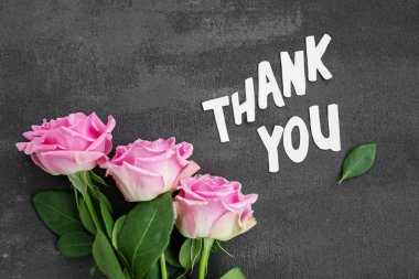 Üç pembe gül beyaz harflerin yanına yerleştirilip koyu dokulu arka planda 