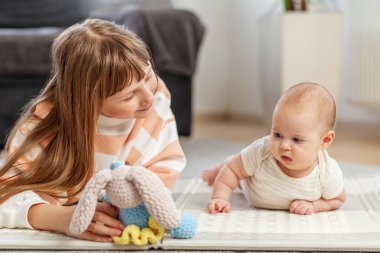 Oyun hasırındaki bir bebek, ablasının sıcacık bir evde karnını doyurduğu yumuşak bir oyuncağa bakar..