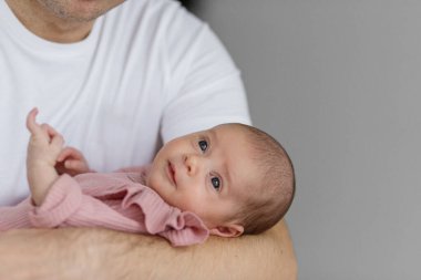 Bir baba, yeni doğmuş bebeğini nazikçe kucağına alır. Her ikisi de rahat, kapalı bir mekanda rahatlar. Yumuşak sabah ışığı, bebeğin tuhaf ifadesini ön plana çıkarıyor ve iç açıcı bir atmosfer yaratıyor..