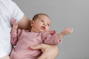 Bir baba, yeni doğmuş bebeğini nazikçe kucağına alır. Her ikisi de rahat, kapalı bir mekanda rahatlar. Yumuşak sabah ışığı, bebeğin tuhaf ifadesini ön plana çıkarıyor ve iç açıcı bir atmosfer yaratıyor..