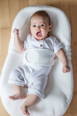 İki aylık bir bebek, yumuşak beyaz ergonomik bir kozada dinleniyor. Üst görünüm