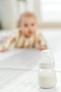 Meraklı bir bebek yerde duran süt şişesine doğru sürünüyor. Oda yumuşak renklerle aydınlanmış, sıcak ve davetkar bir atmosfer yaratıyor oyun zamanı için mükemmel..