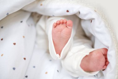 Küçük bebek ayakları, minicik kalplerle süslenmiş rahat ve yumuşak bir battaniyeden dışarı bakıyor. Bebek rahat bir şekilde yuvalanır, narin ayak parmakları ve pürüzsüz derisi sergilenir..