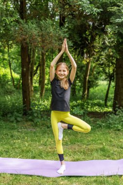 Genç kız orman ortamında yoga ağacı pozu veriyor denge, farkındalık ve doğanın zevkini gösteriyor..