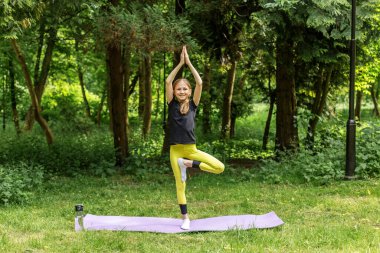Genç kız orman ortamında yoga ağacı pozu veriyor denge, farkındalık ve doğanın zevkini gösteriyor..