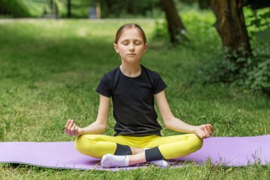 Kız gündüz vakti parkta yoga yapıyor. Kız temiz ve yeşil ortamda yoga yapıyor..