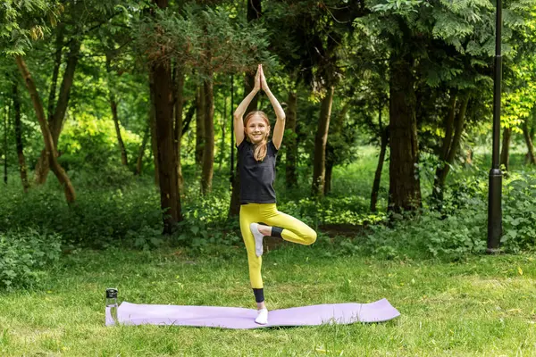 Genç kız orman ortamında yoga ağacı pozu veriyor denge, farkındalık ve doğanın zevkini gösteriyor..