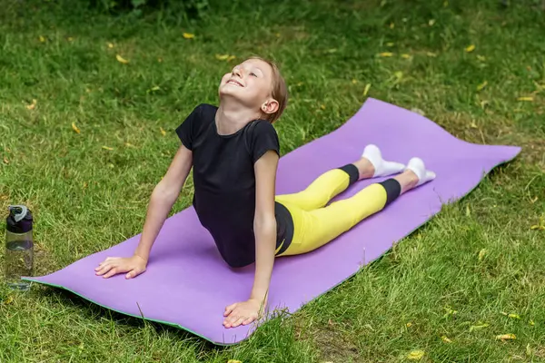 Genç bir kız ormanda bir minder üzerinde yoga pozu veriyor. Sırtını uzatıyor ve sakin bir şekilde yukarı bakıyor..