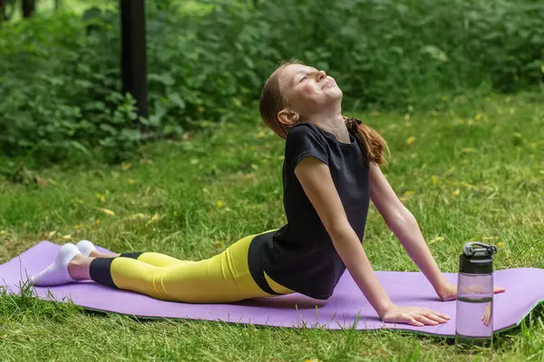Genç bir kız ormanda bir minder üzerinde yoga pozu veriyor. Sırtını uzatıyor ve sakin bir şekilde yukarı bakıyor..