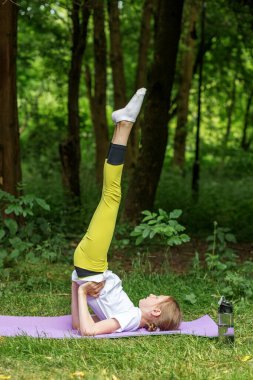 Bir ergen, ağaçlarla çevrili yemyeşil bir alanda yoga pozu veriyor. Denge ve konsantrasyona odaklanan çocuk zindelik ve refah için esneme hareketleri yapıyor..