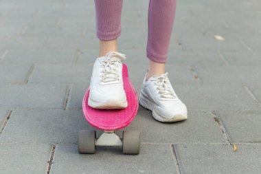 Yakından bakıldığında, pembe bir kaykayın üzerinde beyaz spor ayakkabılarla yürümeye hazır biri görülüyor..