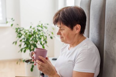 Yaşlı kadın rahat bir şekilde yatağında oturuyor, sıcak bir içki tutuyor ve güzel, rahat bir yatak odasında huzurlu bir anın tadını çıkarıyor..