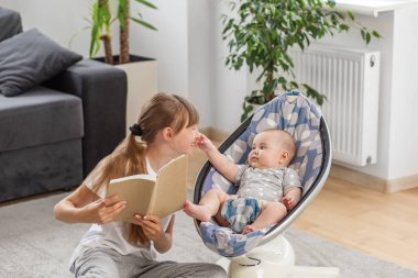 Küçük bir kızın, evde yüksek sesle kitap okurken ablasının yüzüne dokunmak için uzandığı sevimli bir an..