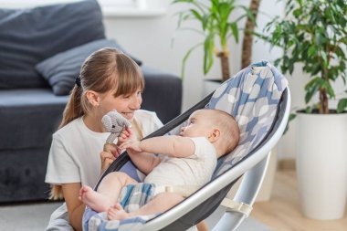 Gülümseyen kız küçük gri doldurulmuş bir oyuncak kullanarak kardeşiyle oynuyor. Yumuşak doğal ışık ve bitkilerle iç mekanlar.