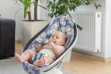 Bebek, el yapımı bir fil çıngırağını çiğnerken modern bir rockçıda rahatça yatıyor. Yumuşak ışıkla sakin bir ortam.