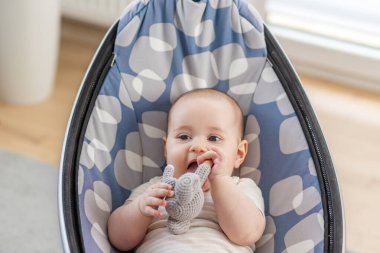 Yastıklı bir rockçının içinde el yapımı bir filin çıngırağını çiğneyen bir bebeğin yakın çekimi. Parlak iç mekan ve doğal ışık..