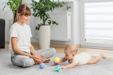 Büyük ablası gülümseyerek izliyor. Küçük erkek kardeşi, oturma odasında karnını doyururken renkli desenli topları keşfediyor..