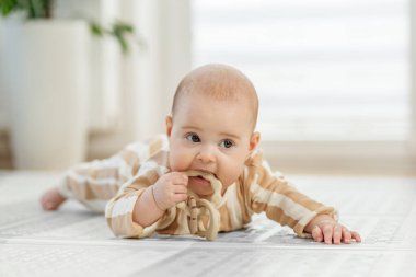 Çizgili pijamalı bir bebek yerde yatar, diş çıkarma sahnesinde bir oyuncağı çiğner, diş etlerini keşfeder ve sakinleştirir..