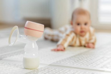Arka planda bir bebeğin öne doğru uzandığı, sütle doldurulmuş elektrikli göğüs pompasına yakın plan..