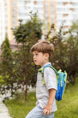 Yeşil yerleşim yerlerinde küçük sırt çantalı genç bir çocuk, tuhaf bir ifadeyle ileriye bakıyor..