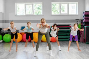 Eğitmen, bir spor salonundaki spor salonunda denge, güç ve koordinasyon üzerine çalışan bir grup genç kızı yönetiyor..