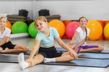 Üç genç kız yoga ya da esneklik kursunda bacak esnetmenin keyfini çıkararak, hareketlilik ve duruşu eğlenceli bir ortamda teşvik ediyor..