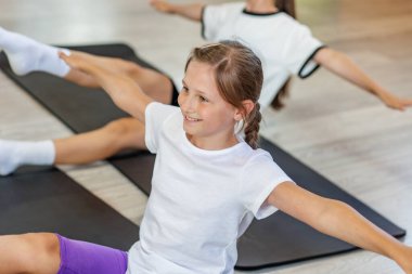 Mutlu genç kız vücut egzersizi sırasında kollarını ve bacaklarını açıyor. Spor salonu ortamında denge ve koordinasyon çalışması yapıyor..