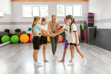 Gülümseyen kızlar ve dans hocaları bir çember oluşturuyorlar, motivasyon takımında el ele tutuşuyorlar. Dersten önce ya da sonra spor salonunda toplanıyorlar..