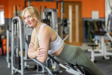 Kendine güveni tam genç bir kadın modern spor salonunun arka koltuğunda vücut, kalça ve bel kaslarını güçlendiriyor..