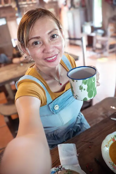 Bir kadın, cep telefonuyla selfie çekerken geleneksel bir Cava tenekesi tutuyor..