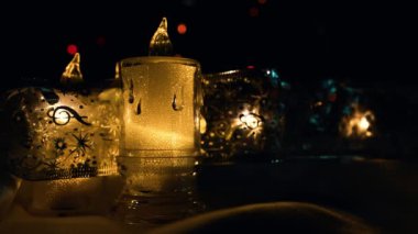 Sarı ışık saçan elektrikli mumlar, parlak kurdelelerle, koyu bir arka planla ve parıldayan Noel ışıklarıyla çevrilidir. Metin ile doldurulabilecek boş bir alan var. 