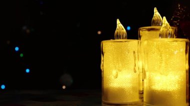 Sarı ışık saçan elektrikli mumlar karanlık bir arka plan ve parıldayan Noel ışıklarına karşı. Metin ile doldurulabilecek boş bir alan var. 