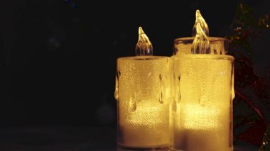 Sarı ışık saçan elektrikli mumlar karanlık bir arka plan ve parıldayan Noel ışıklarına karşı. Metin ile doldurulabilecek boş bir alan var. 