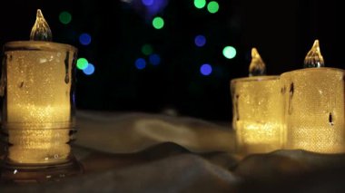 Sarı ışık saçan elektrikli mumlar karanlık bir arka plan ve parıldayan Noel ışıklarına karşı. Metin ile doldurulabilecek boş bir alan var. 