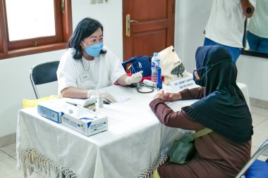Doktor, bir sağlık merkezindeki hastaya danışır. Masada gerekli tıbbi malzemeler bulunur ve kapsamlı bakım sağlanır..